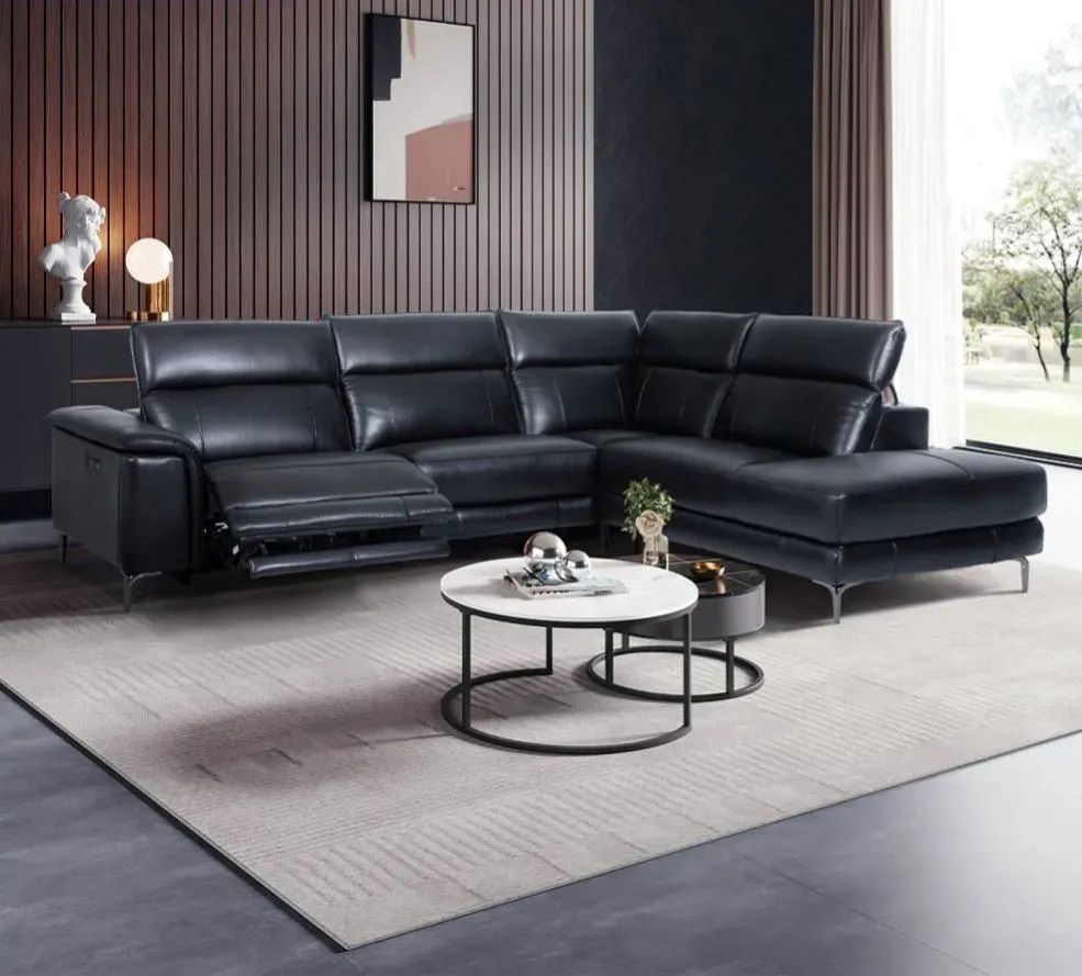 A living room with a black leather sectional couch and two coffee tables.
