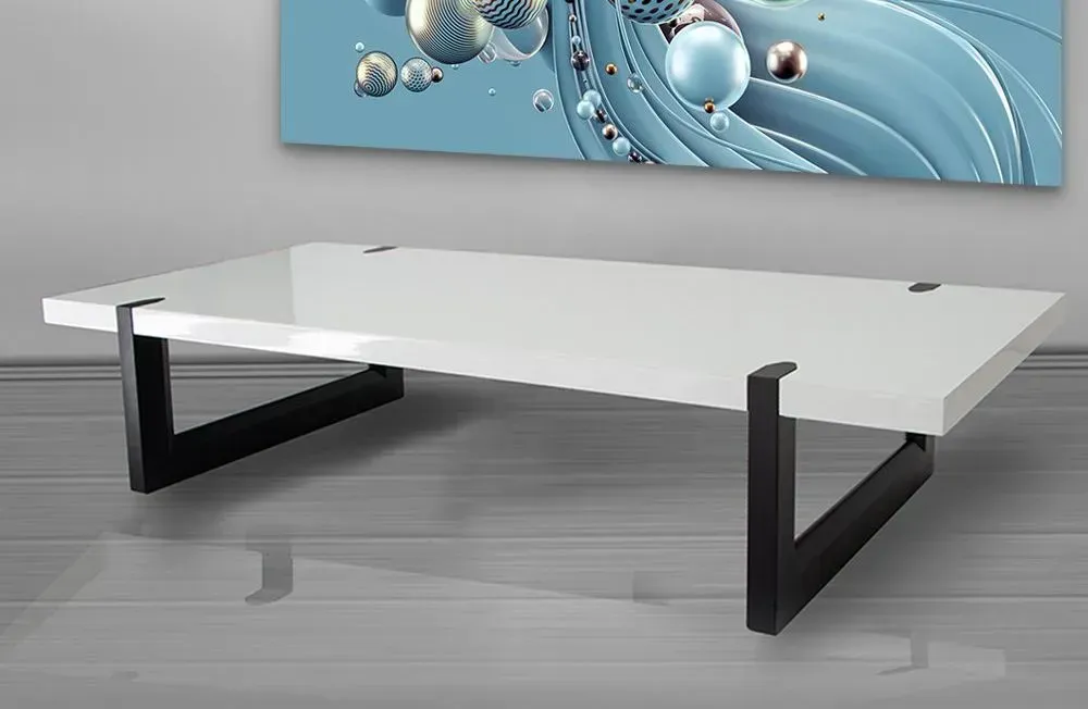 A white coffee table with black legs is sitting under a painting on the wall.