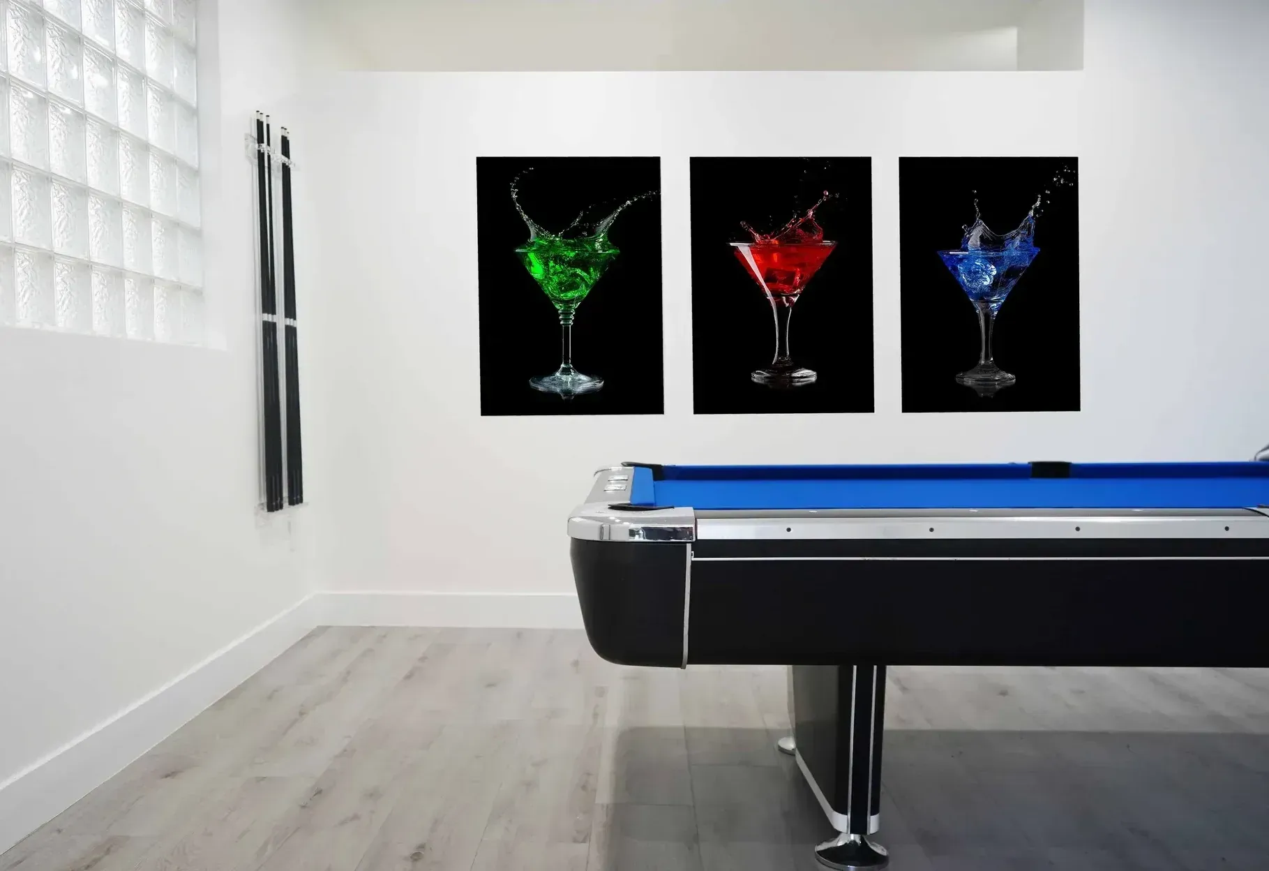 A pool table in a room with three pictures of martini glasses on the wall