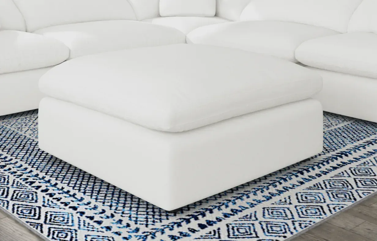 A white ottoman is sitting on top of a blue and white rug next to a white sectional couch.