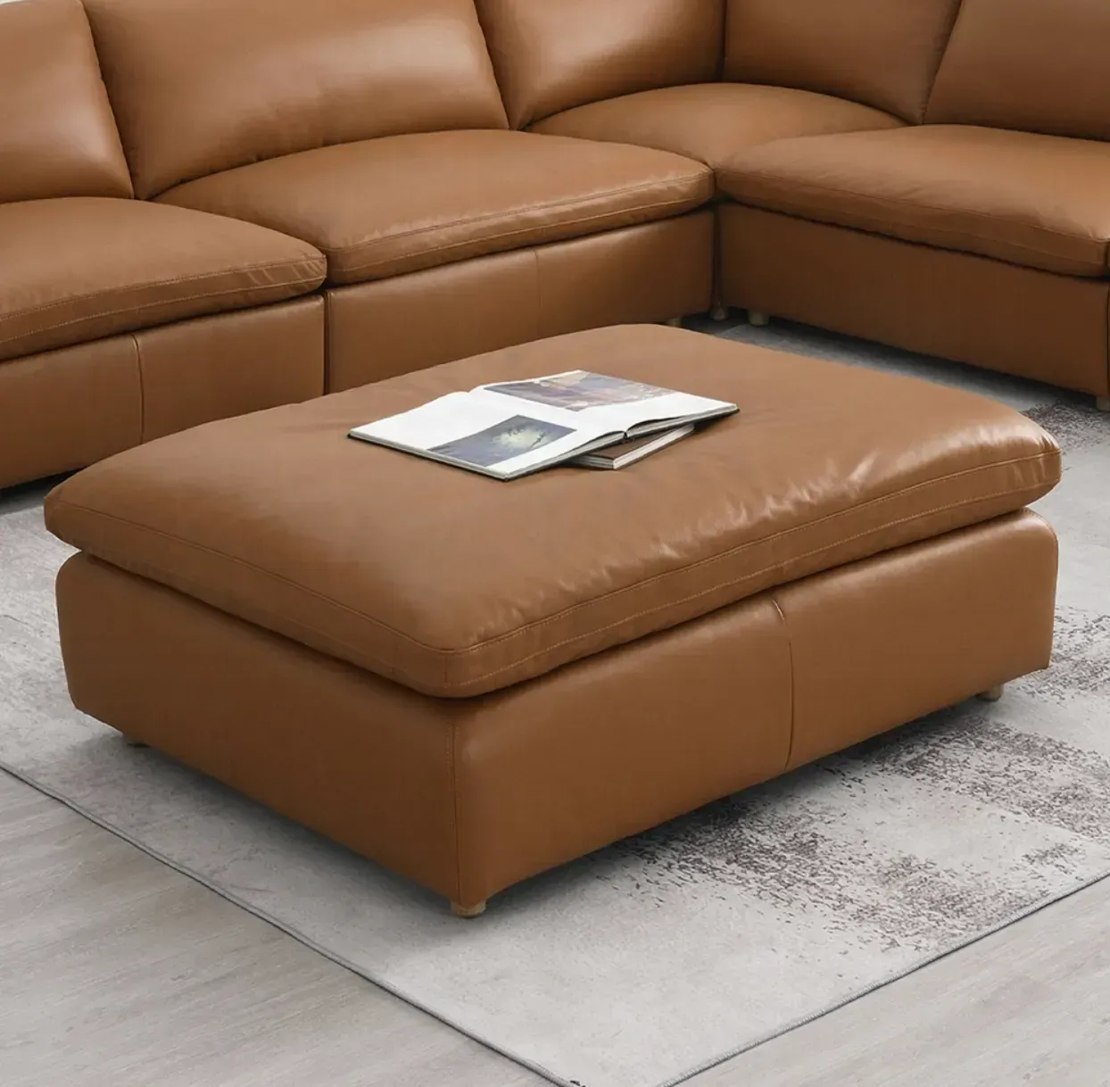 A brown leather ottoman is sitting in front of a brown sectional couch.