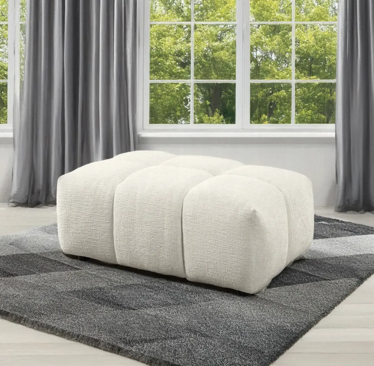 A white ottoman is sitting on a rug in front of a window.