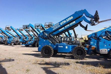 A row of blue construction vehicles are parked in a lot.