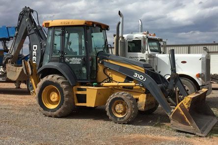 A yellow and black backhoe is parked next to a white truck.