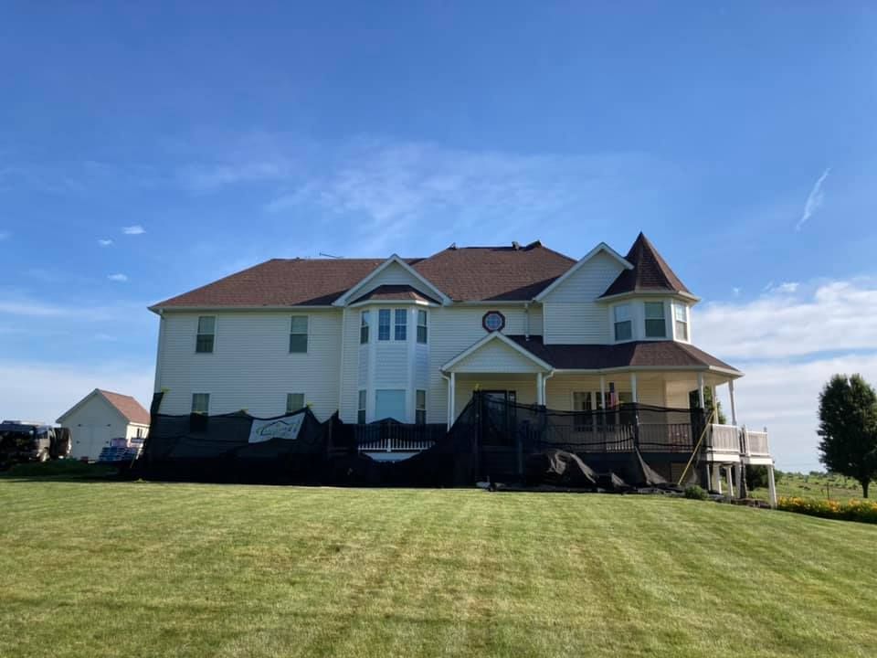 A large white house with a red roof is sitting on top of a lush green field.