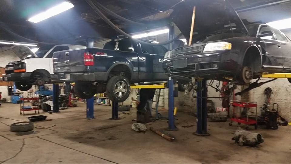 Three vehicles on hydraulic lifts inside an auto repair shop with tools and equipment scattered across the concrete floor.