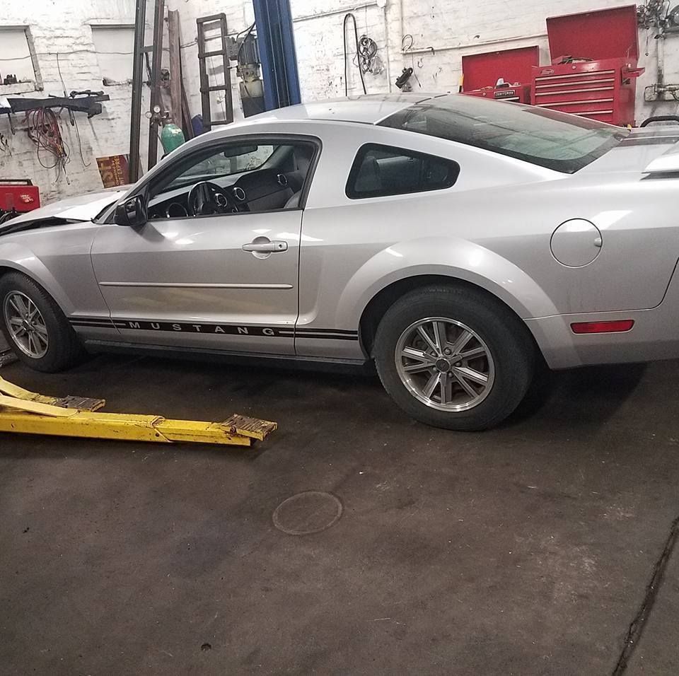 A silver Ford Mustang parked inside an auto repair shop with a yellow car lift visible in the foreground.