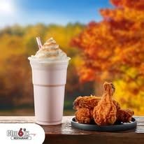 A milkshake with whipped cream and fried chicken drumsticks on a plate against a fall foliage background.