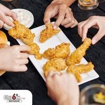 People reaching for fried chicken on a white platter at a table.