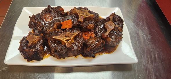 Plate of cooked oxtail stew, pieces in a rich dark sauce.
