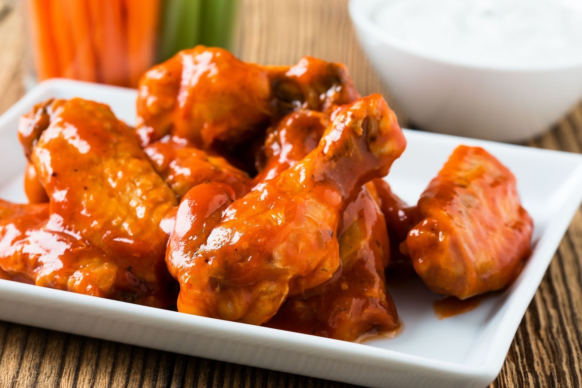 Buffalo wings with sauce on a white plate, alongside carrots, celery, and dip.