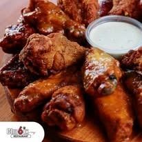 Close-up of a plate of chicken wings, some glazed, served with a side of dipping sauce.