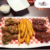 Chicken wings and fries on a checkered platter with dipping sauce and a small bowl.
