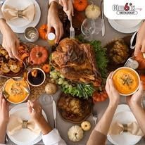 Thanksgiving table, hands reaching for food, turkey, pumpkins, and a variety of dishes.