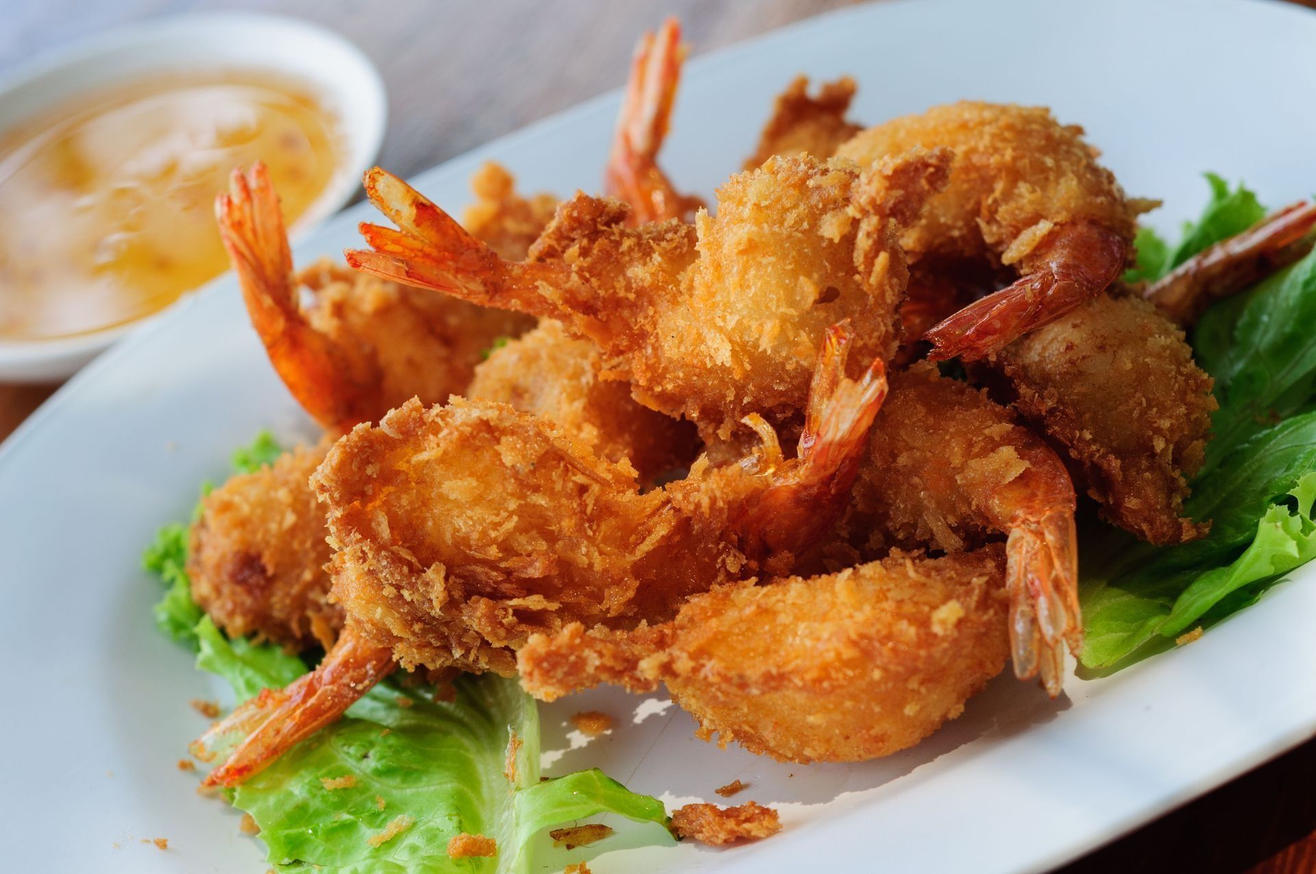 Fried shrimp with dipping sauce on a bed of lettuce, served on a white plate.