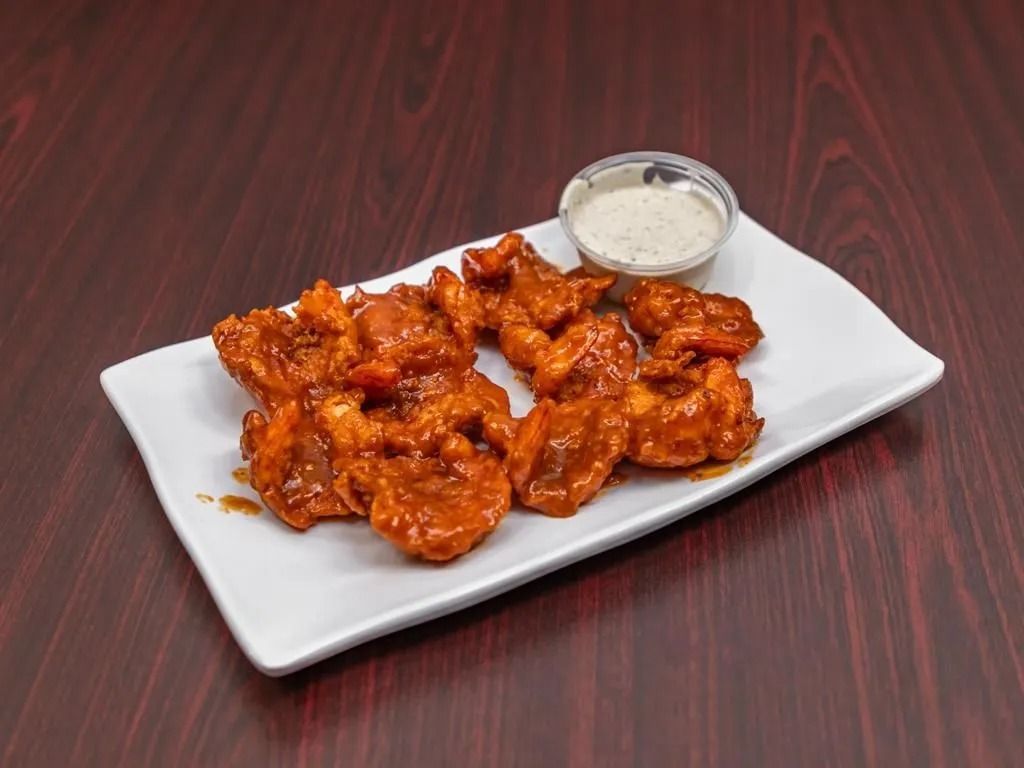 Buffalo chicken bites on a white plate with a side of ranch dressing on a wooden table.