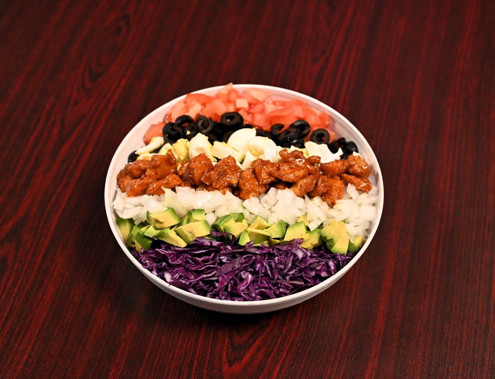 Bowl of food with layers of ingredients: red cabbage, avocado, rice, chicken, mozzarella, olives, tomato.