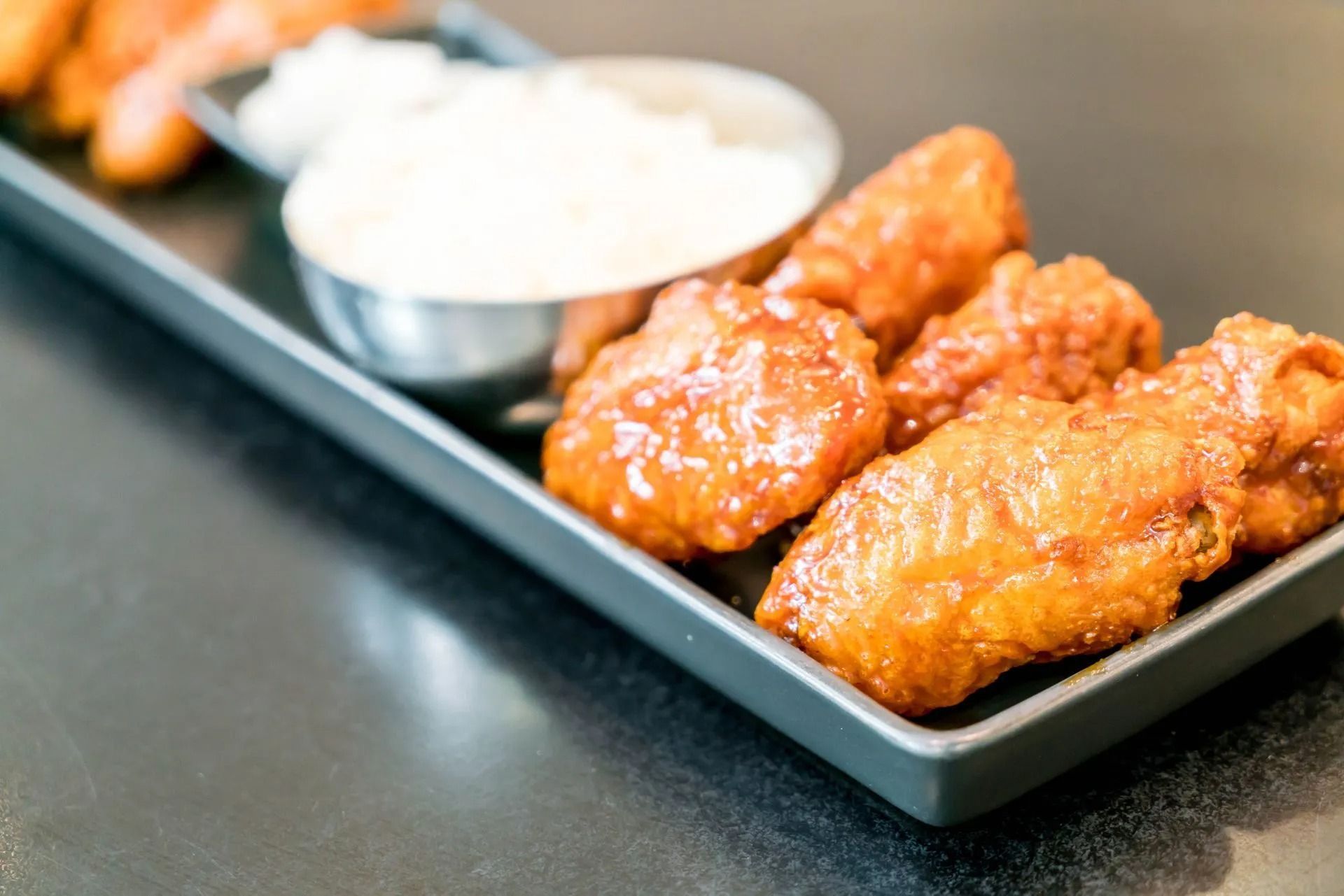 Chicken wings with sauce, served on a black tray with white dipping sauce.