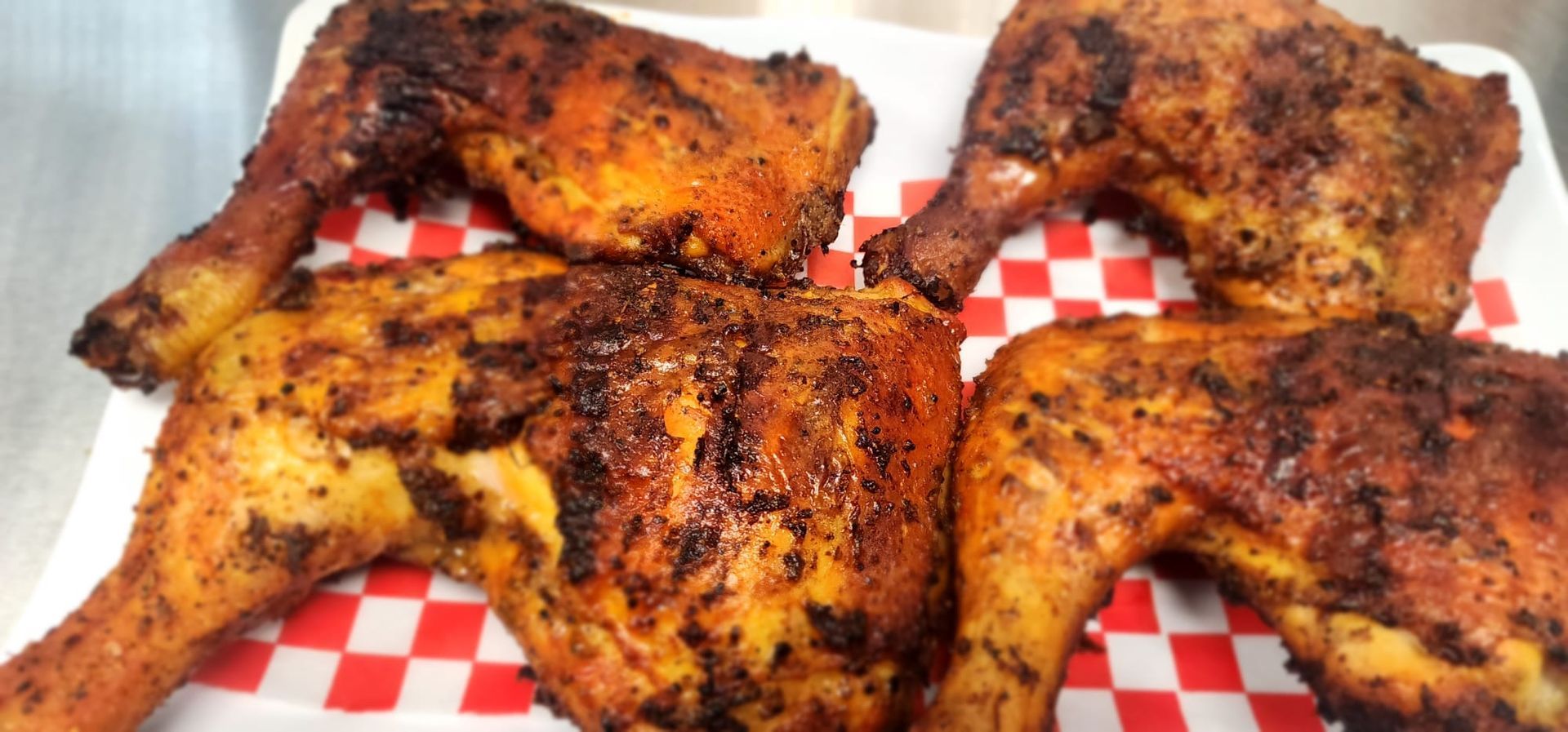 Grilled chicken leg quarters on a red and white checkered plate.