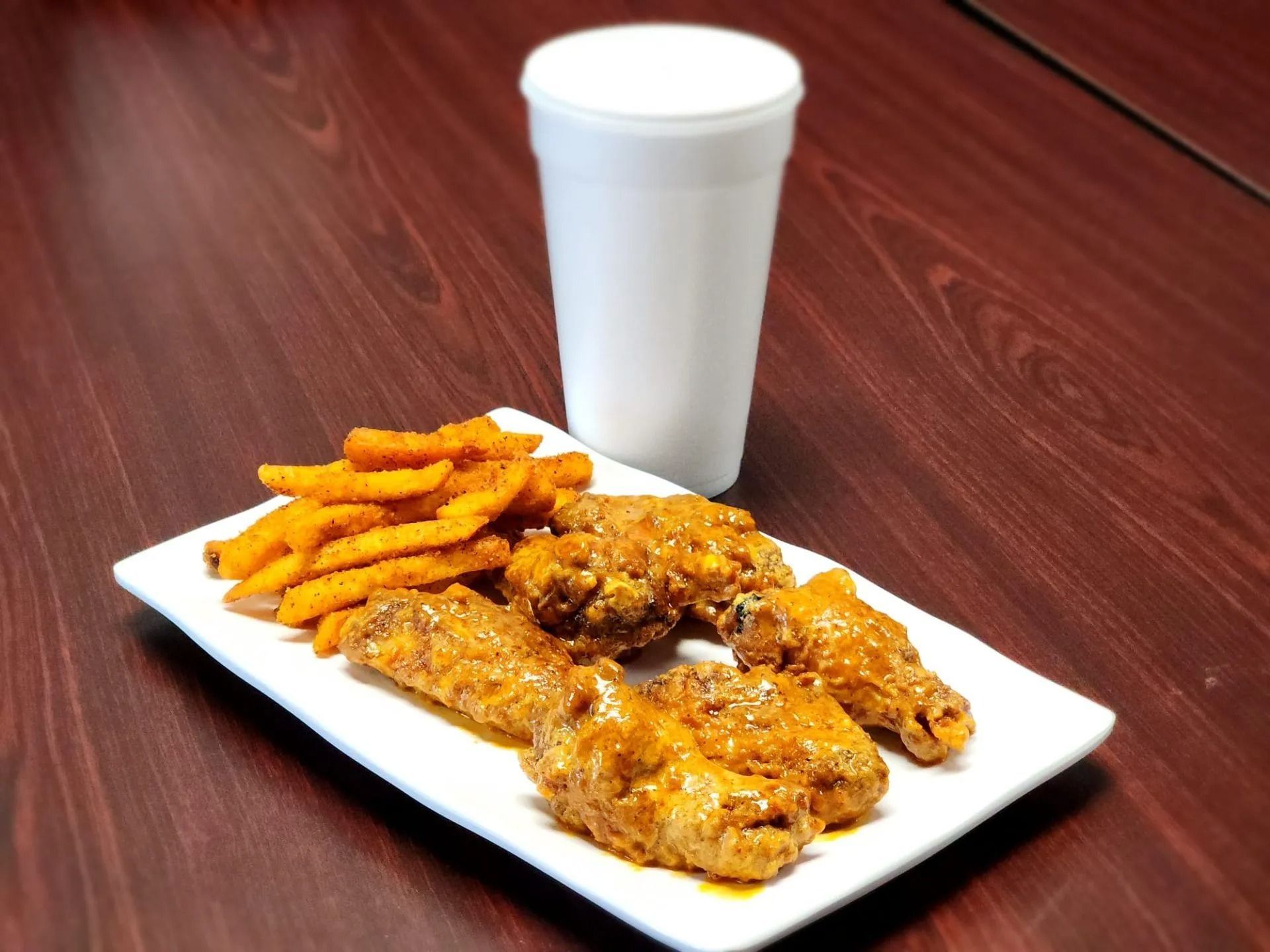 Plate of fried chicken wings and fries with a white cup, on a wood table.