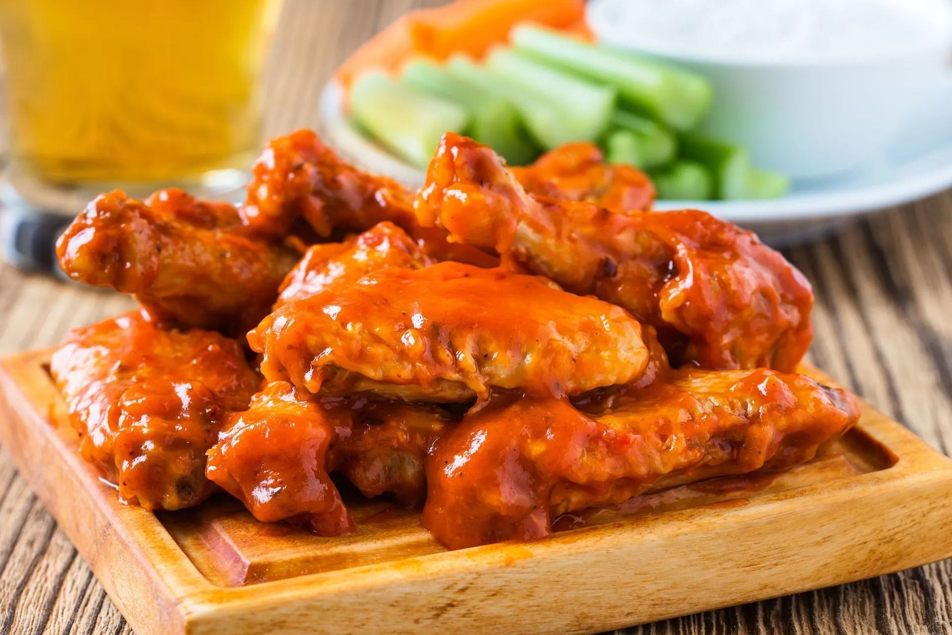 Buffalo wings in red sauce on a wooden board with celery, carrots, and dip.