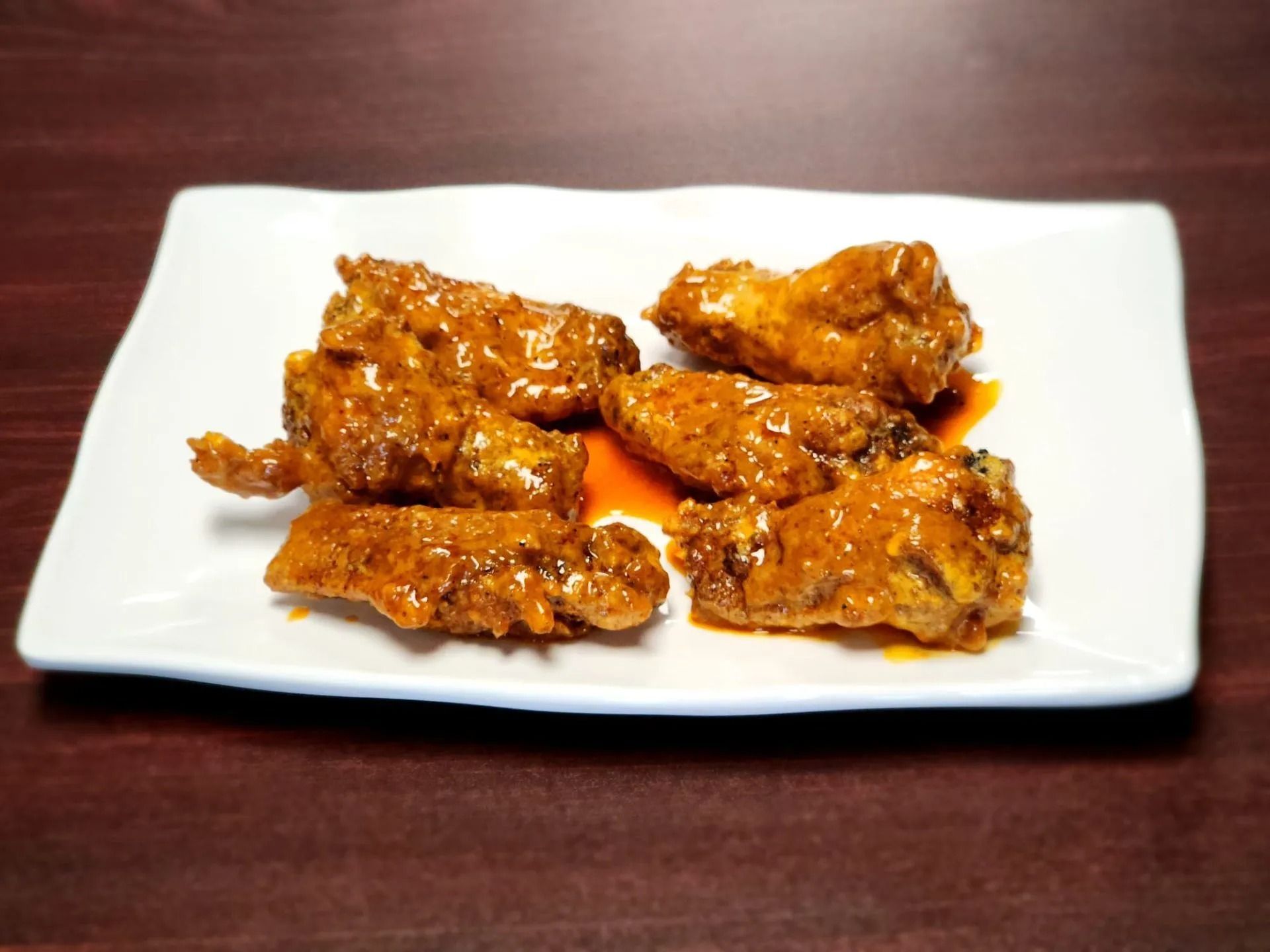 Buffalo wings on a white plate, coated in sauce on a wood surface.