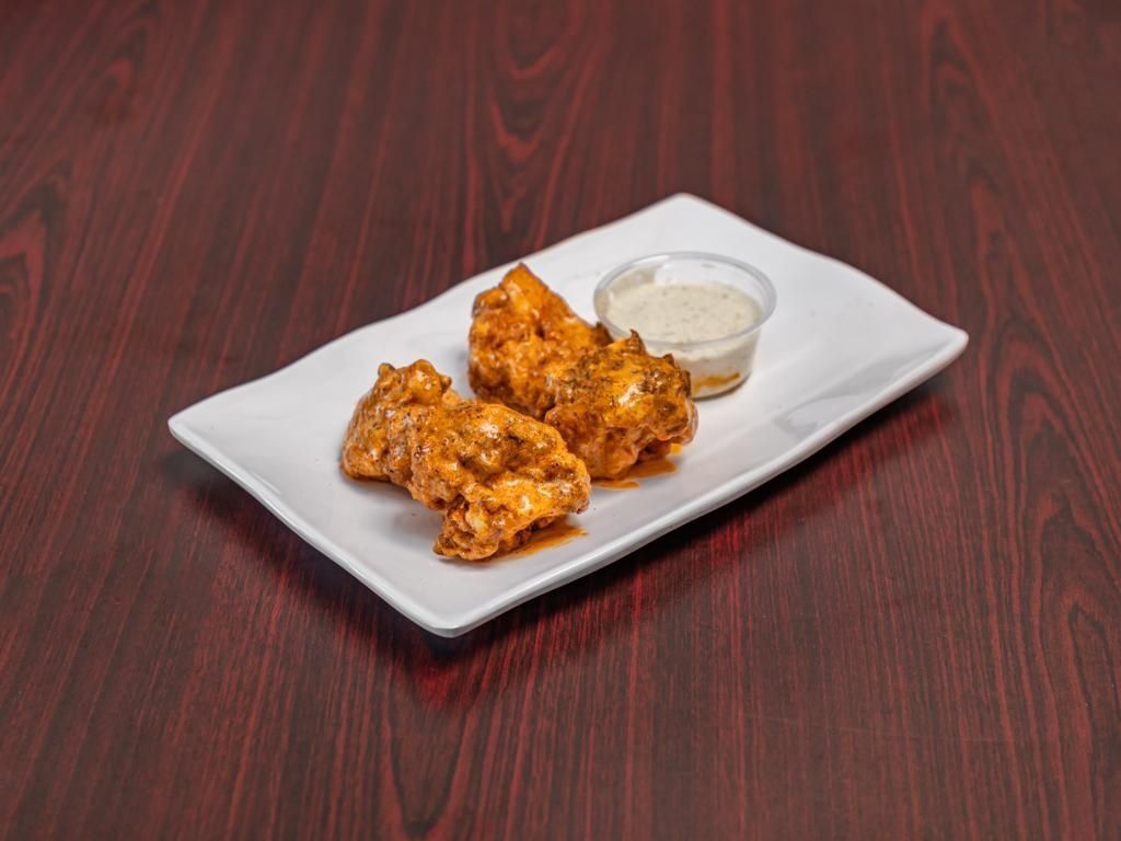 Chicken wings with sauce and dipping sauce on a white plate, placed on a wooden table.