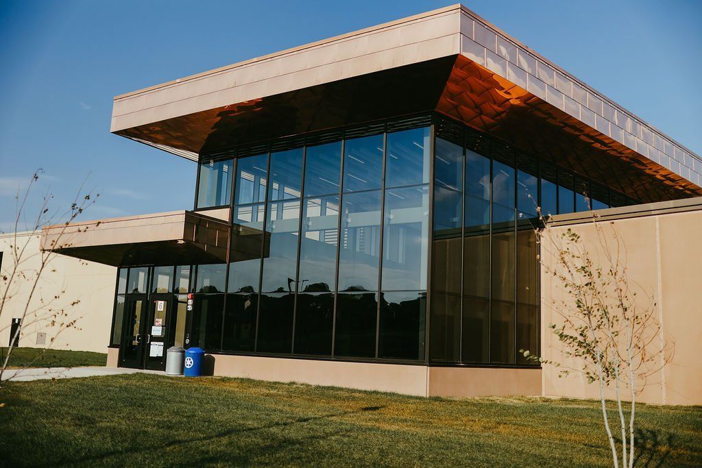Modern building with copper-colored roof and large glass windows reflecting a blue sky.