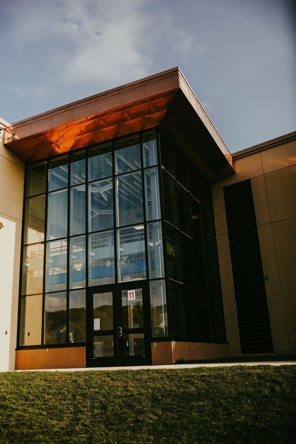 Modern building with large glass windows and brown roof, set against a cloudy sky.