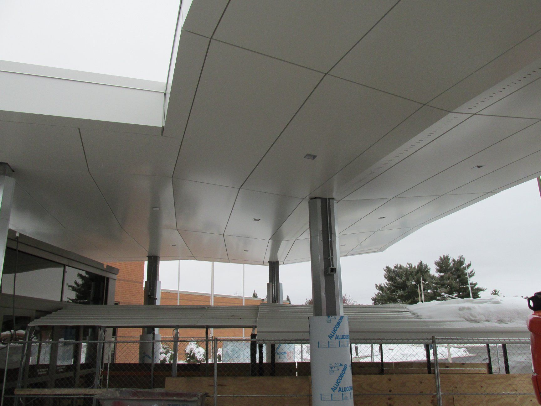 White canopy with a modern design, supported by gray pillars, over a partially built structure.