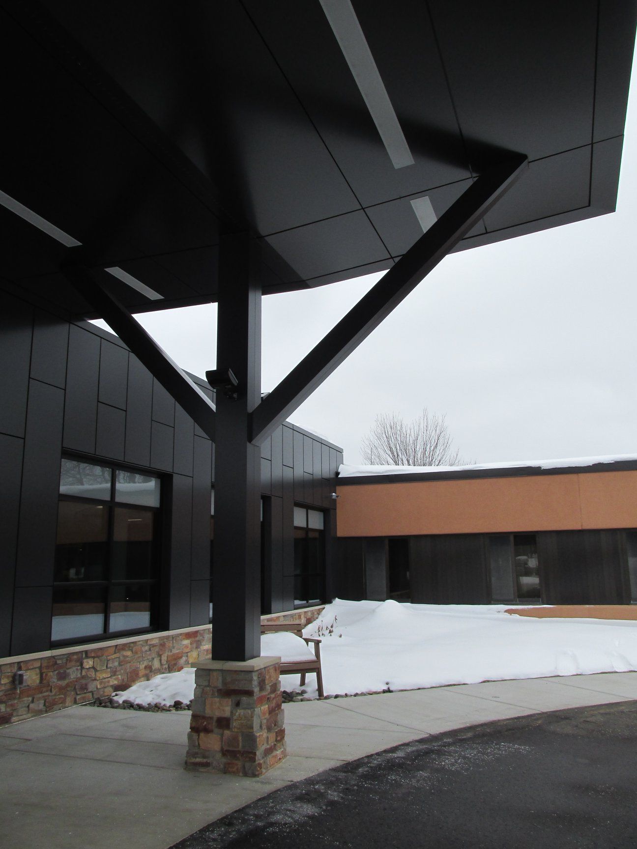 Black building with a canopy supported by a post and braces. Snow covers the ground.