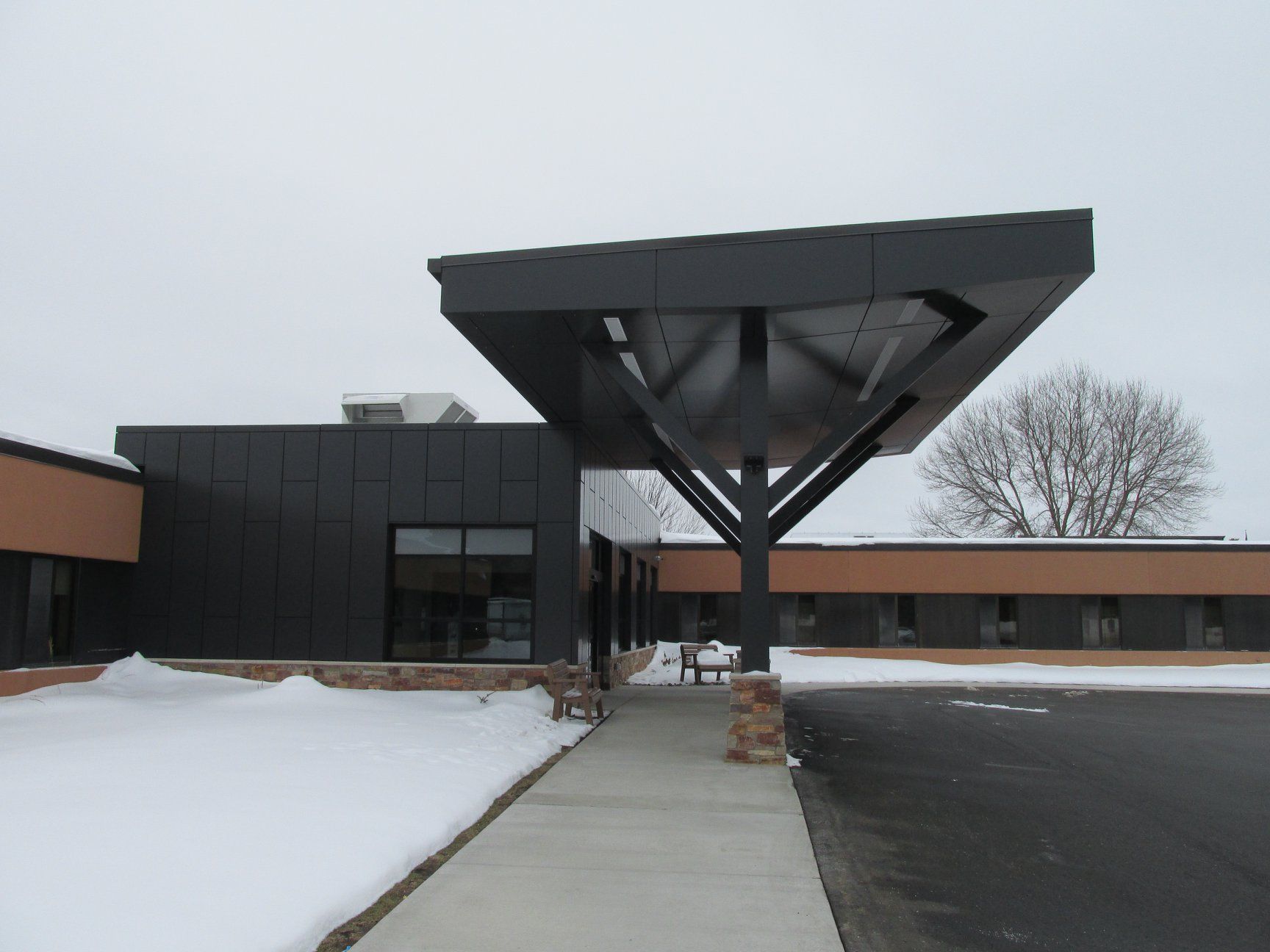 Modern building with dark gray canopy over entrance, snow on ground.