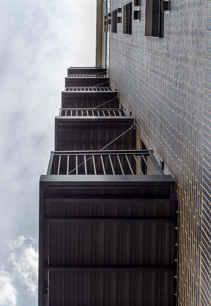 Exterior view of a tall building with multiple dark balconies extending out from the brick wall, cloudy sky in background.