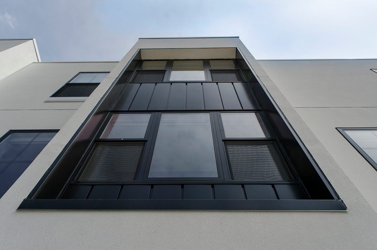Exterior of a modern building with a tall window featuring dark trim and reflective glass.
