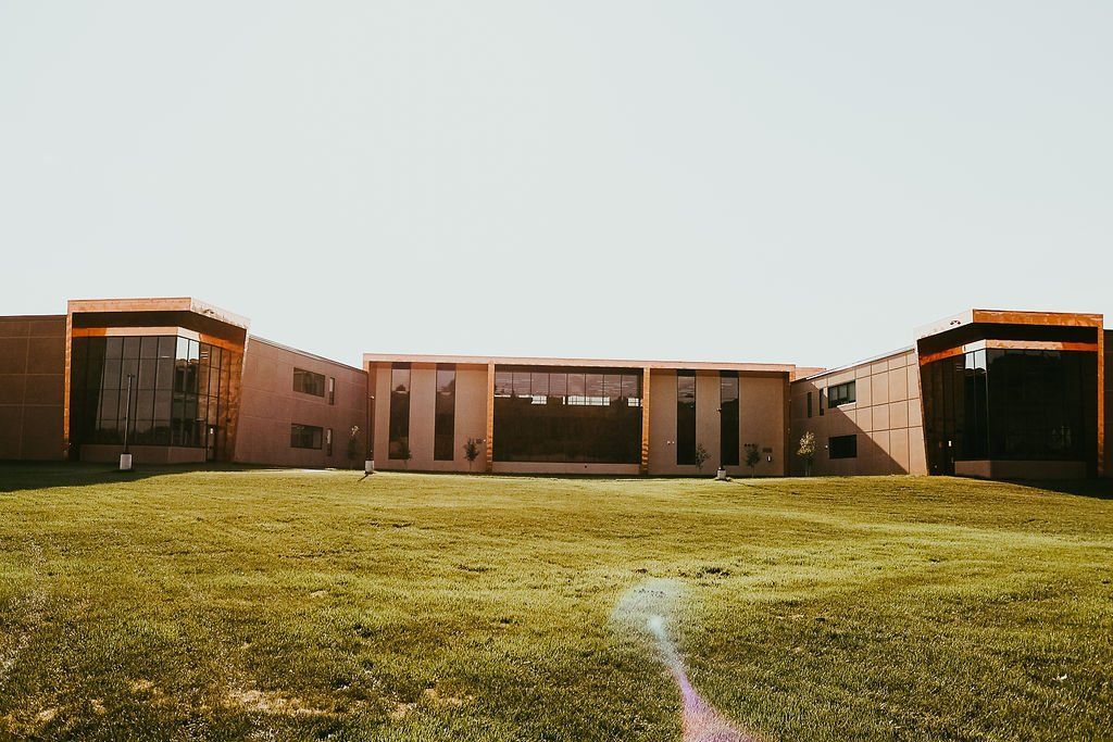 A modern, brown brick building with large windows is set on a grassy lawn under a bright sky.