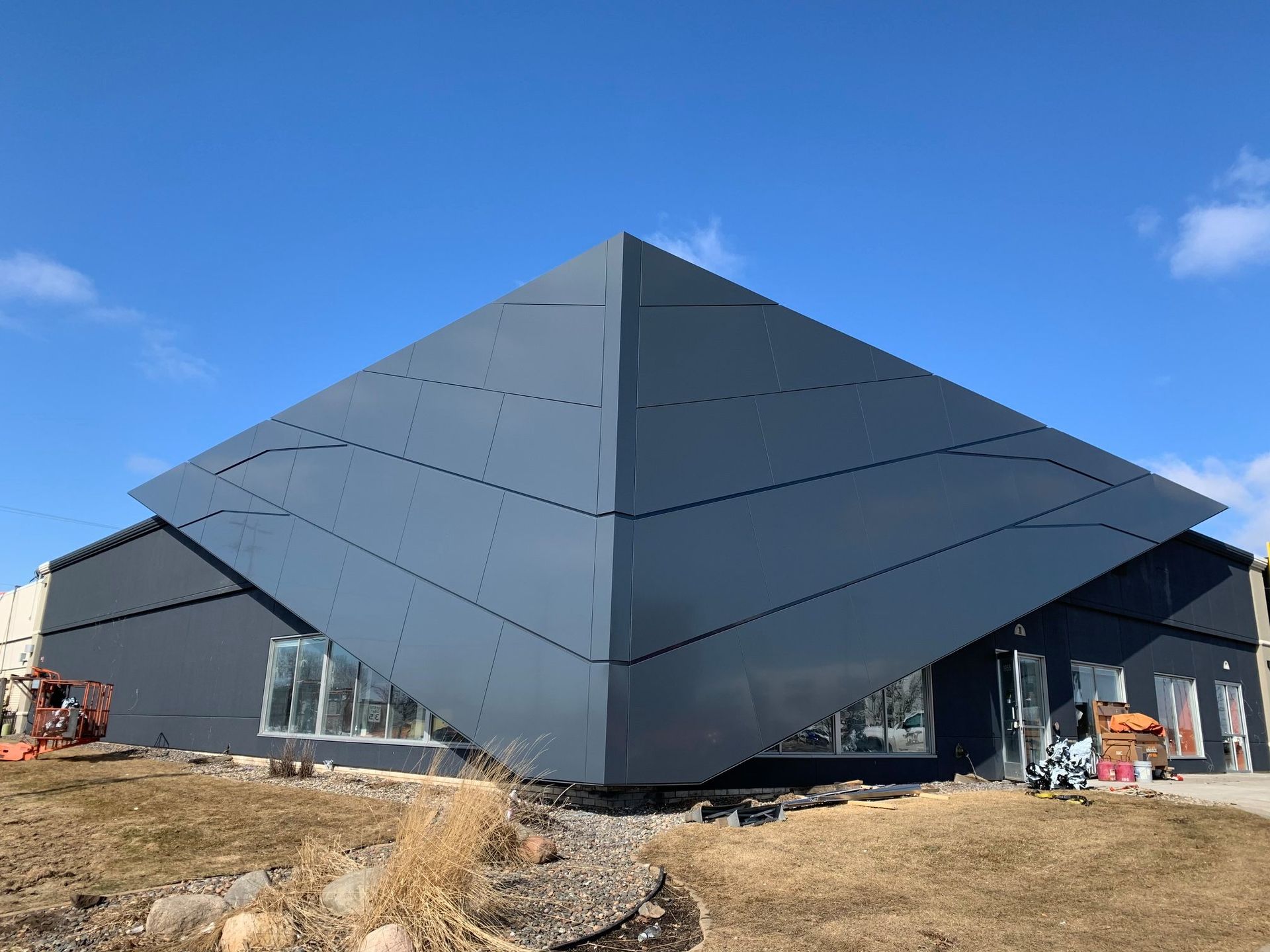 Dark gray building with a large, diamond-shaped, metallic structure extending from the roof against a blue sky.