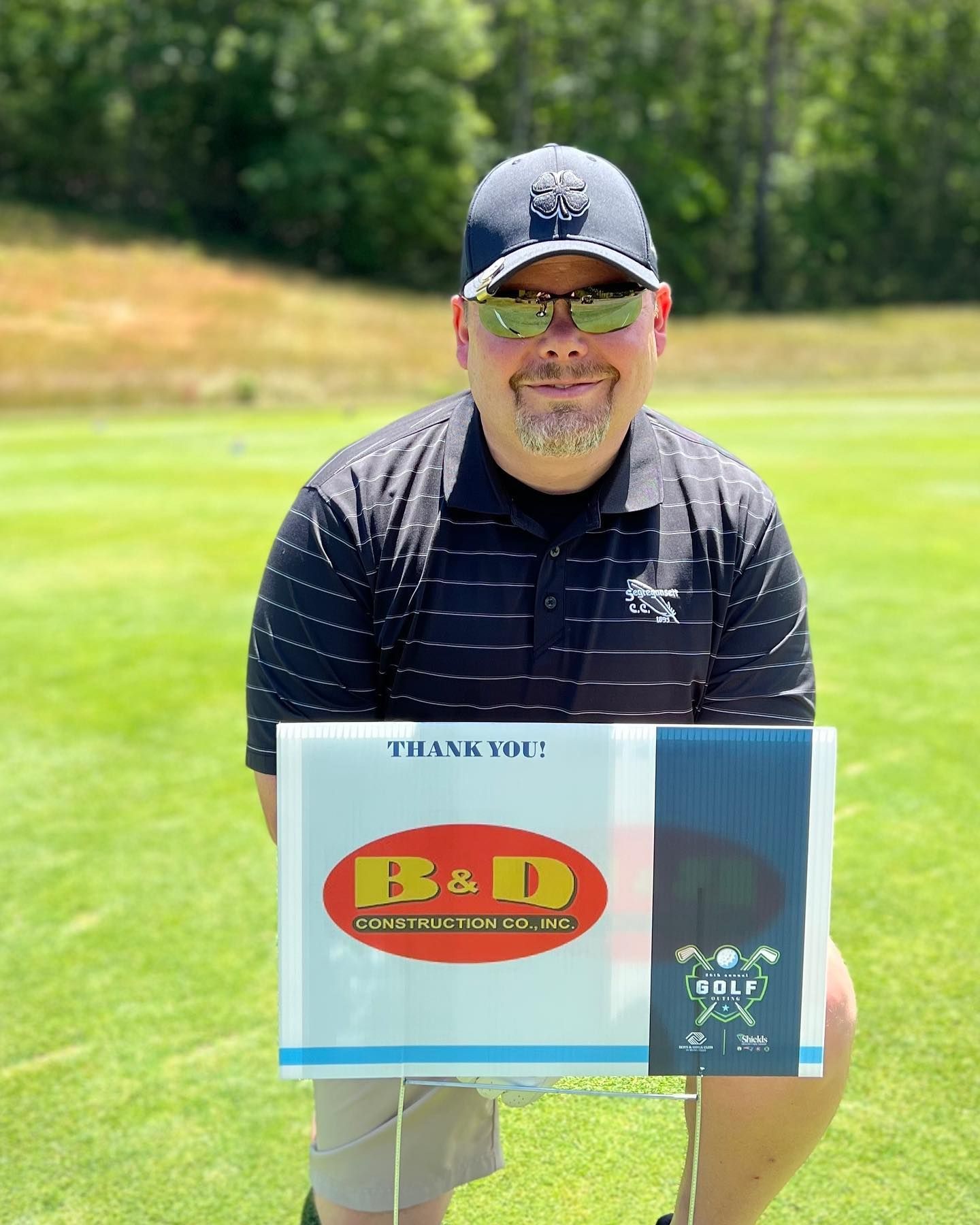 A man is kneeling on a golf course holding a thank you sign.