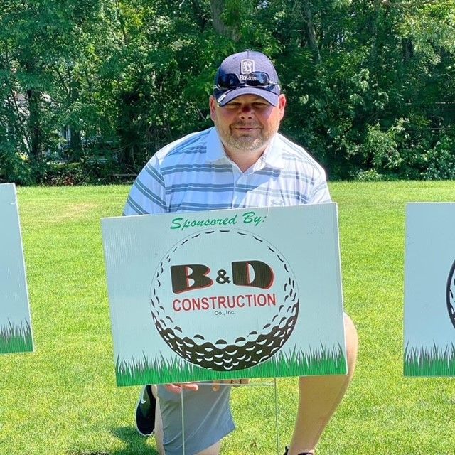A man holding a sign that says b & d construction.