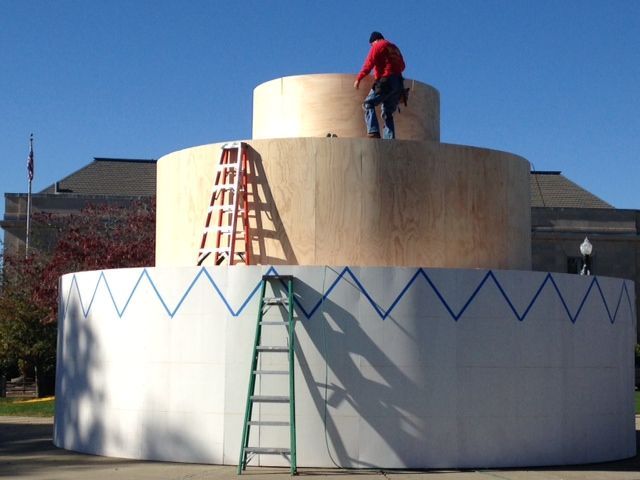 A man is standing on top of a large cake design.