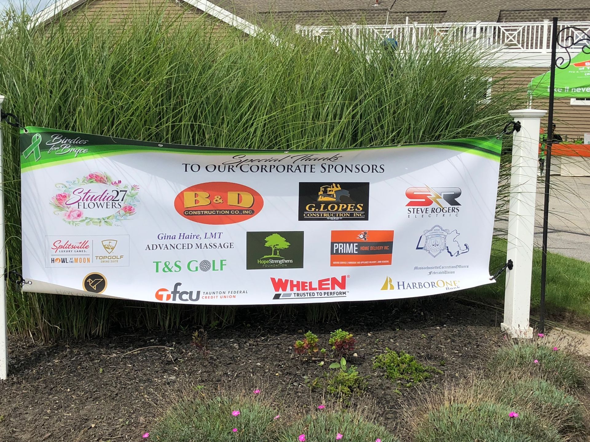 A banner with logos on it is hanging on a pole in front of a house.