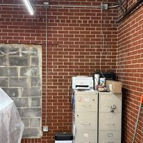 A room with a brick wall , filing cabinets , and a printer.