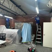A man is standing on a ladder in a room covered in plastic.