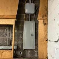 A gray electrical box is hanging on a brick wall in a room.