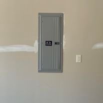 A gray electrical box is hanging on a wall next to a light switch.