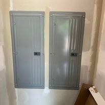 Two electrical panels are hanging on a wall in a room.
