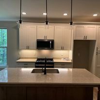 A kitchen with white cabinets , a sink , stove , microwave and refrigerator.