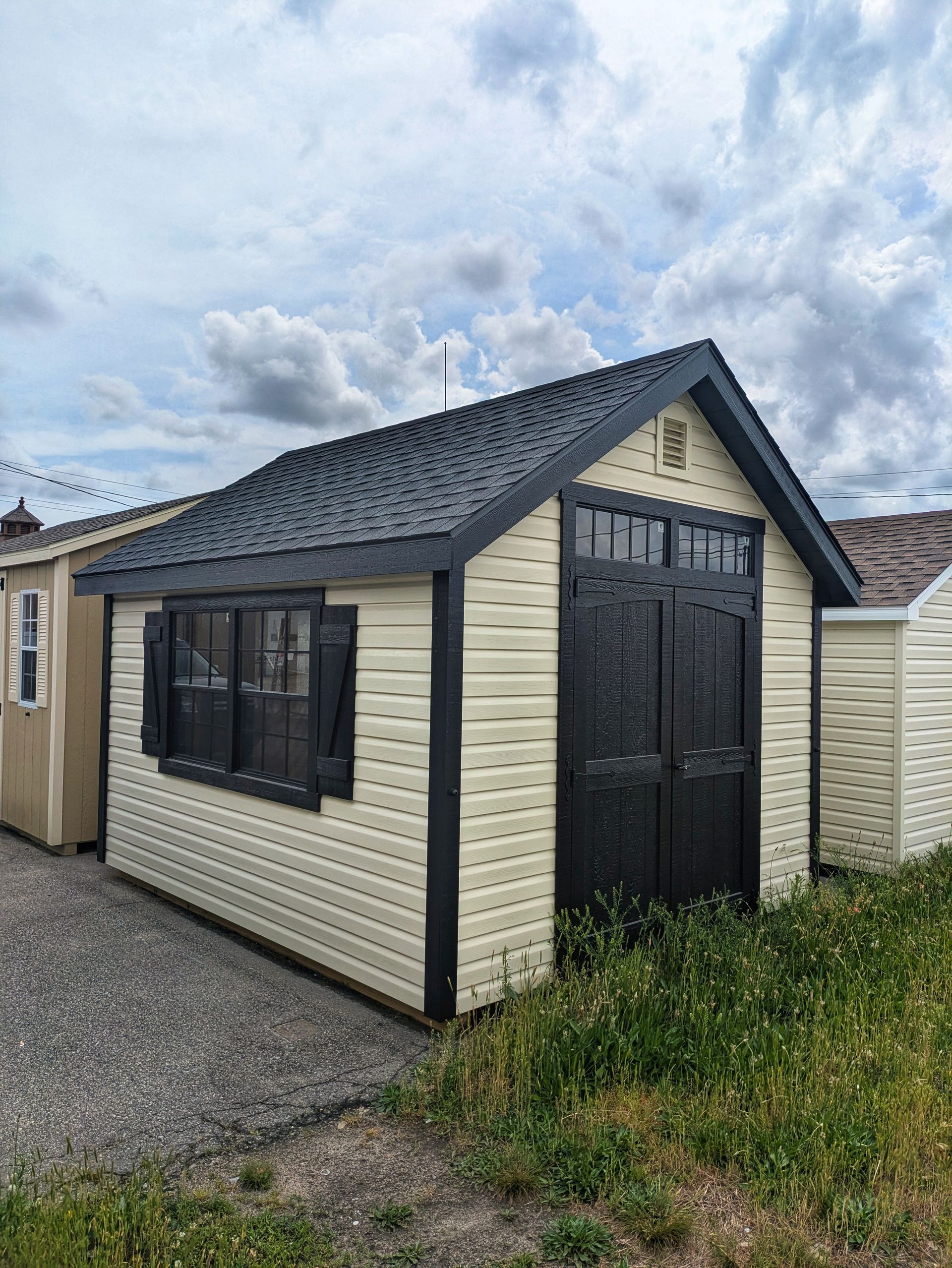 A small white shed with a black roof is sitting in the middle of a grassy field.