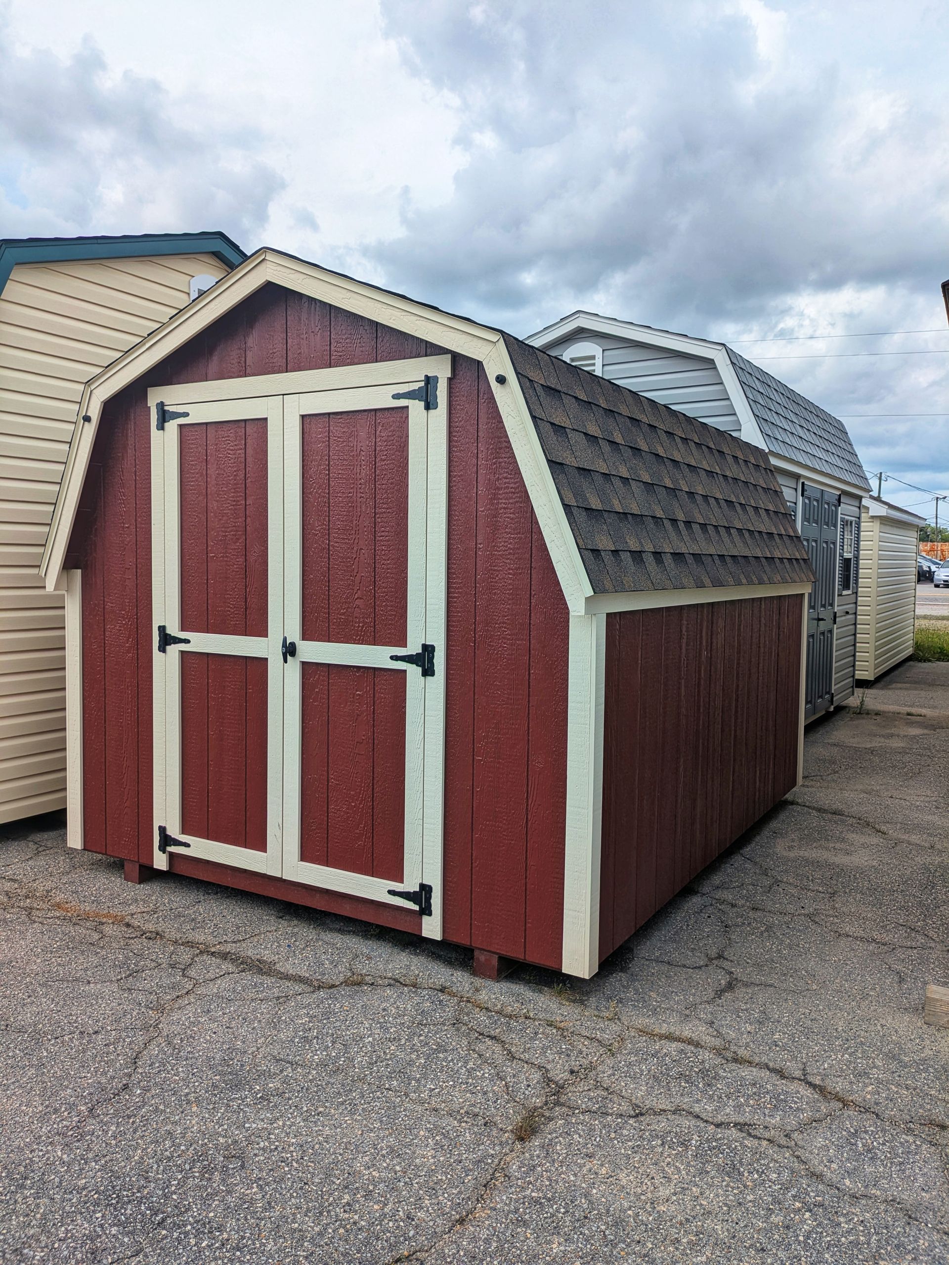 A red barn shed with white trim is sitting on top of a gravel lot.