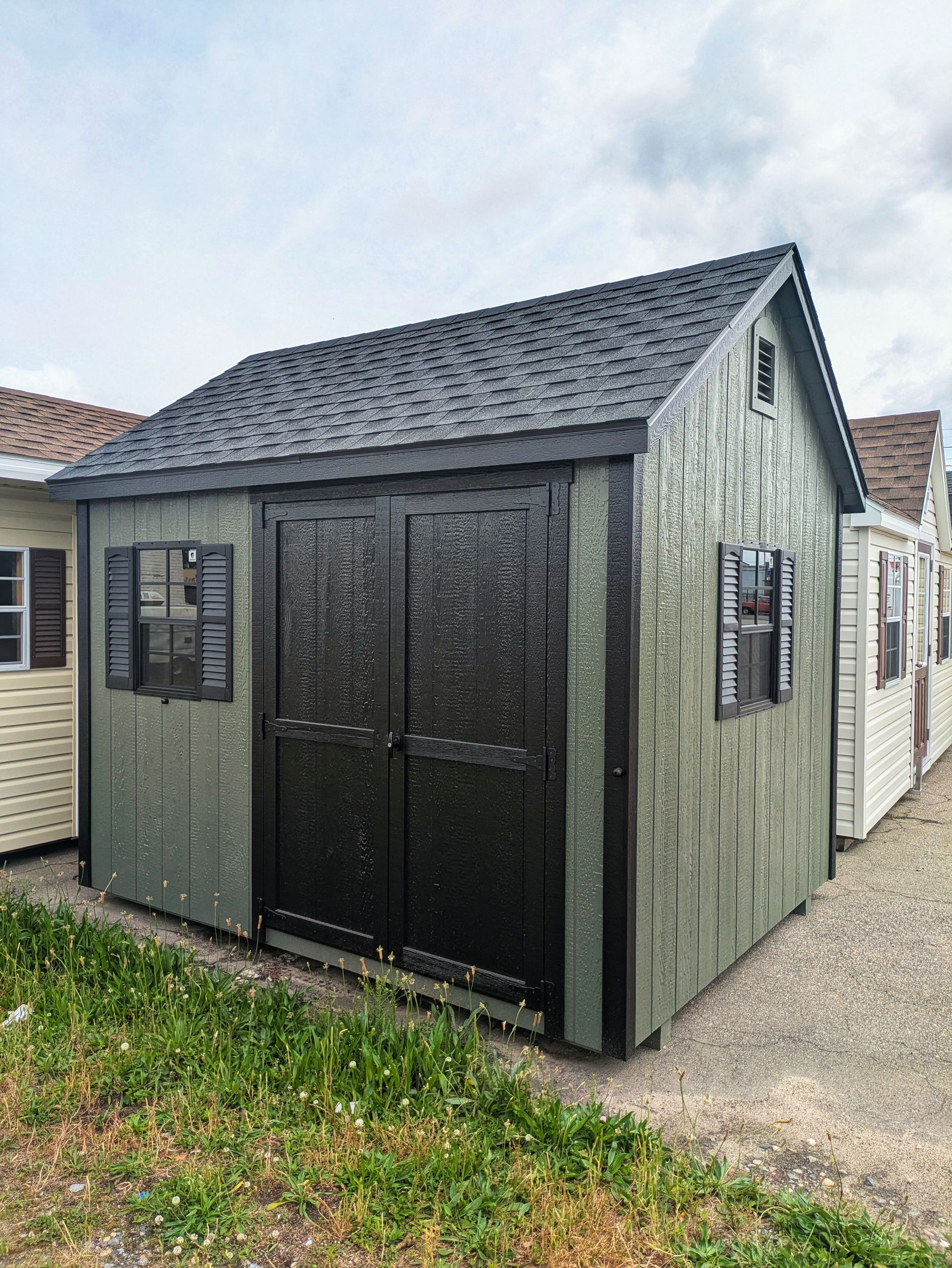 A green shed with black doors and windows is sitting in the grass.