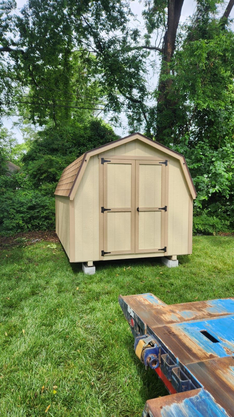 A small wooden shed is sitting on top of a lush green lawn next to a trailer.